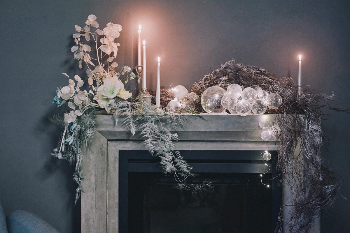 Christmas fireplace decorations, flower arrangement with white Amaryllis, lunaria, Asparagus Plumosus, dyed tulips, dried branches, white candles and transparent baubles, Christmas winter home decoration ideas. Set design by Shanghai florist and set designer Daria Bokova