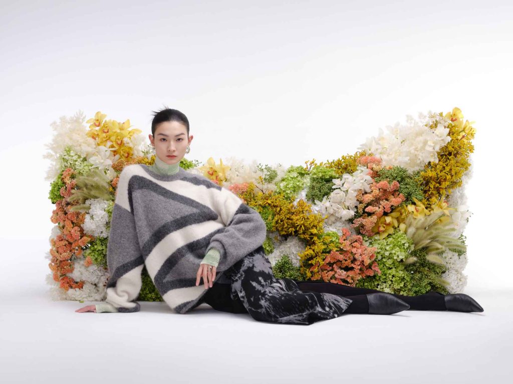 chinese model in autumn sweater and skirt outfit in front of a cat head shaped real flower wall