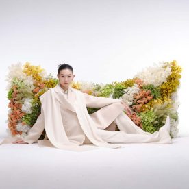 chinese model in light beige coat outfit in front of a cat head shaped real flower wall